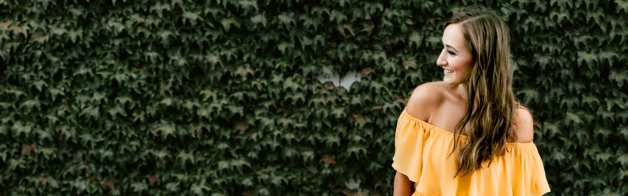 Woman in yellow top against green foliage backdrop.