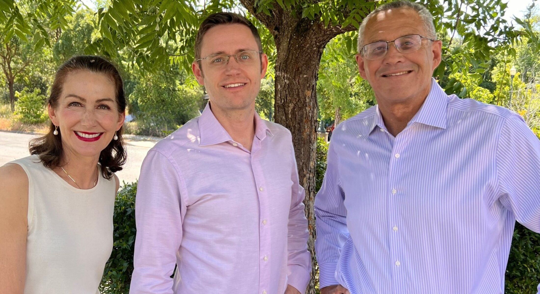 Three smiling individuals standing outdoors together.