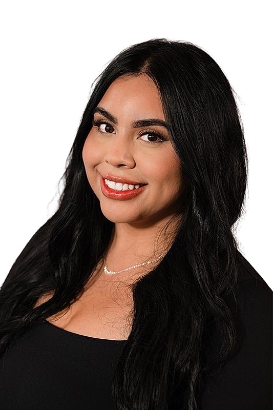 Smiling woman with long black hair against backdrop.